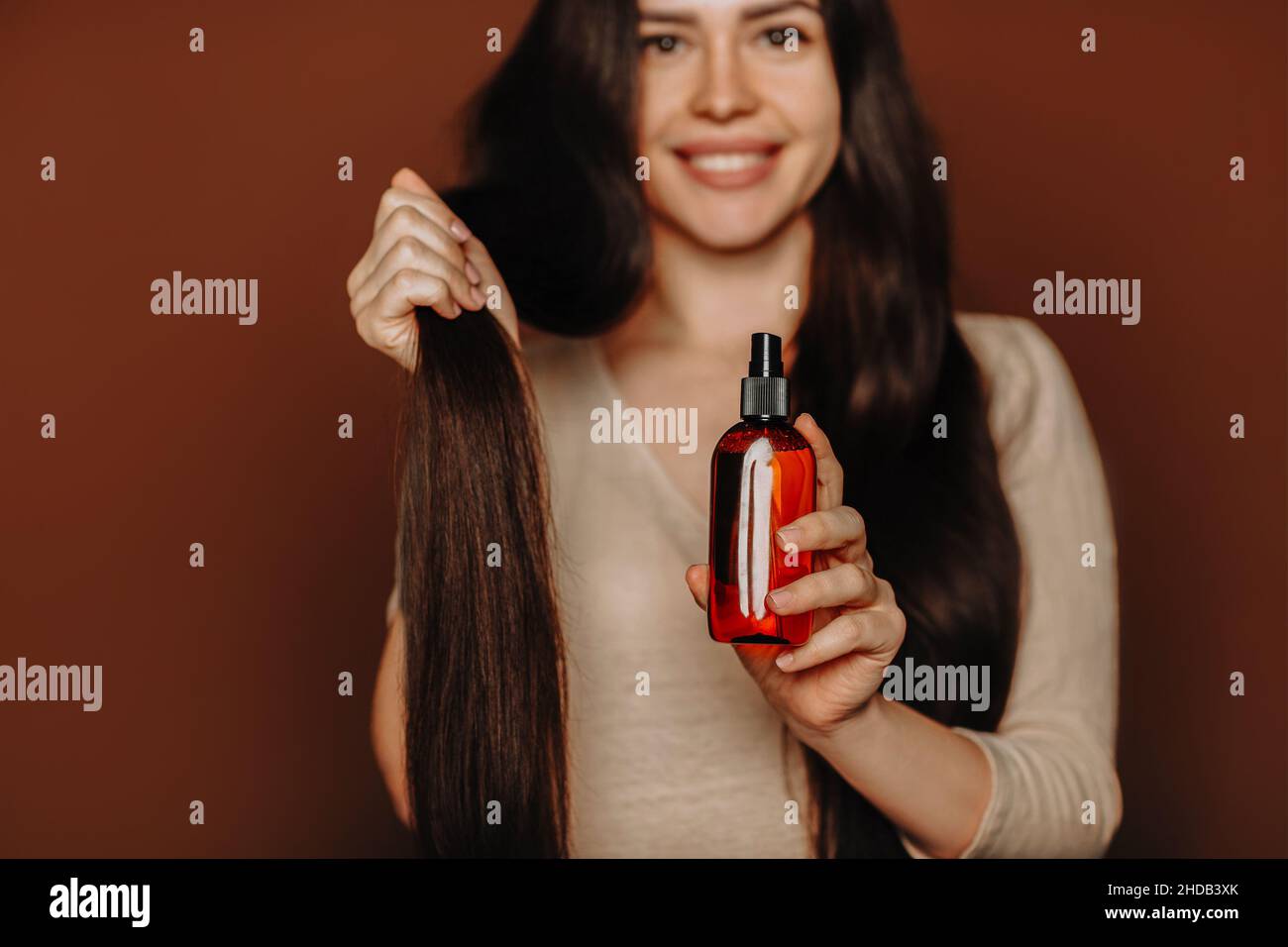 Studioportrait einer glücklichen, zufriedenen Frau, die ihr langes, gesundes braunes Haar hält und Shampoo oder Conditioner der Kamera zeigt, weiblich mit natürlichem Parabe Stockfoto