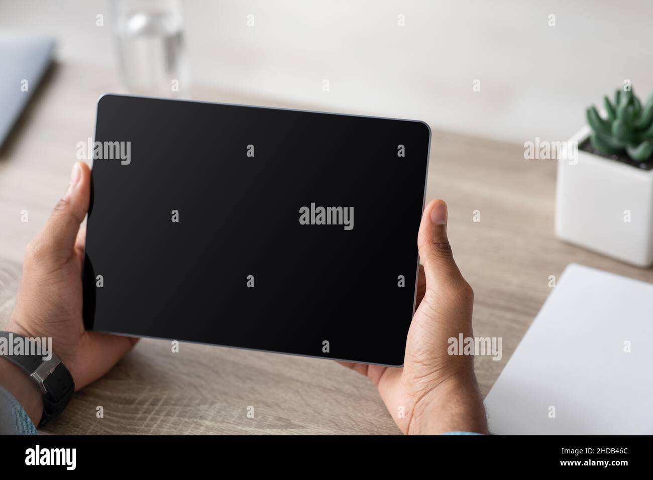Ein junger afroamerikanischer Mann hält ein Tablet mit leerem Bildschirm, arbeitet, schaut sich Videos an, chattet zu Hause am Schreibtisch Stockfoto