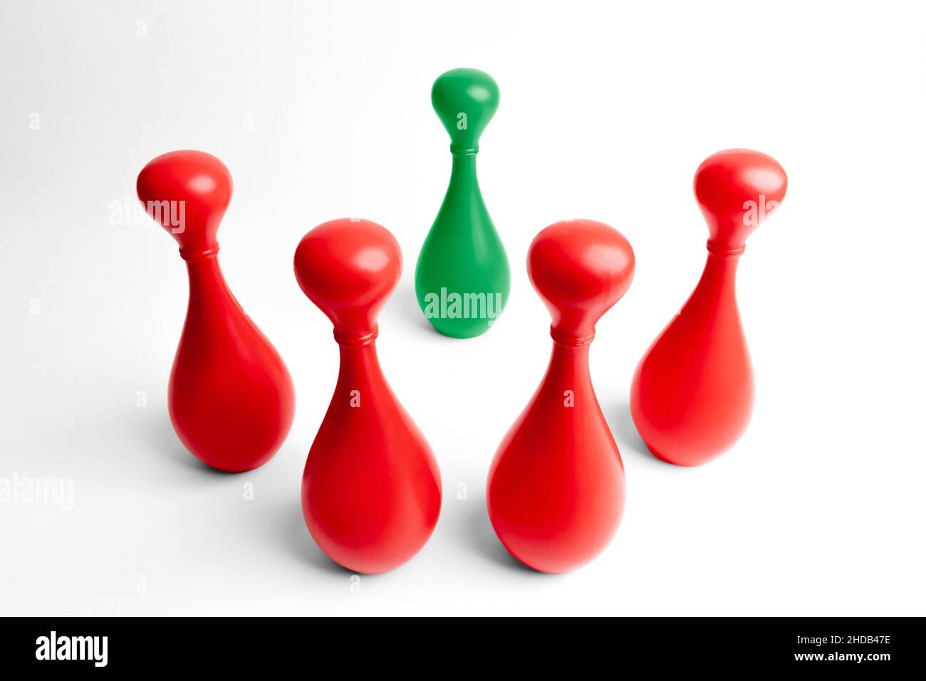 Vier rote Kegeln stehen auf bedrohliche Weise um einen grünen herum. Kampf, anders zu sein. Mobbing verschiedener Menschen. Feindliche Umgebung. Asch Stockfoto
