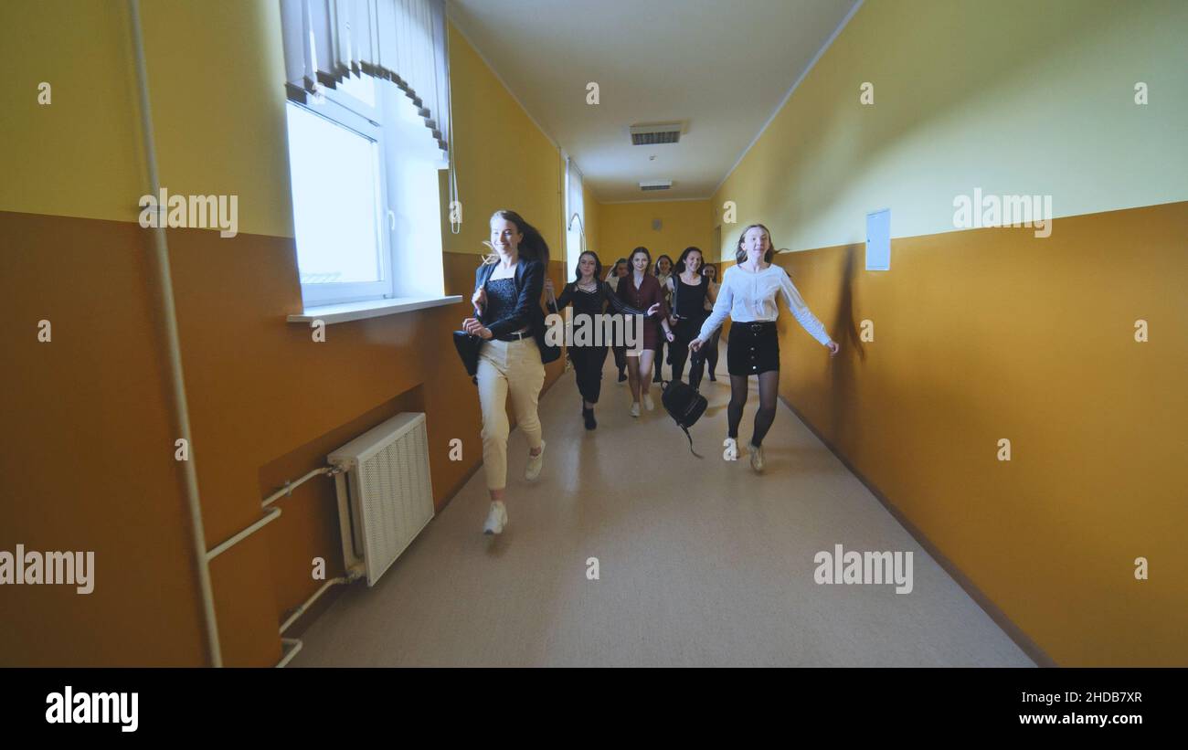 Fröhliche Schülerinnen laufen nach dem Ende des Unterrichts im Schulkorridor. Stockfoto