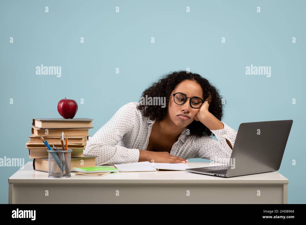 Bildung und Überarbeit. Müde schwarze Studentin, die am Schreibtisch mit Laptop vor blauem Studiohintergrund studiert Stockfoto