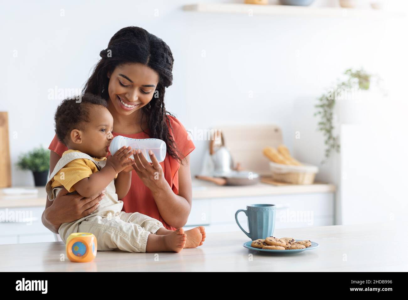 Schwarzer Kleinkind Junge Trinkwasser Aus Flasche Mit Lächelnder Mutter In Der Küche Stockfoto