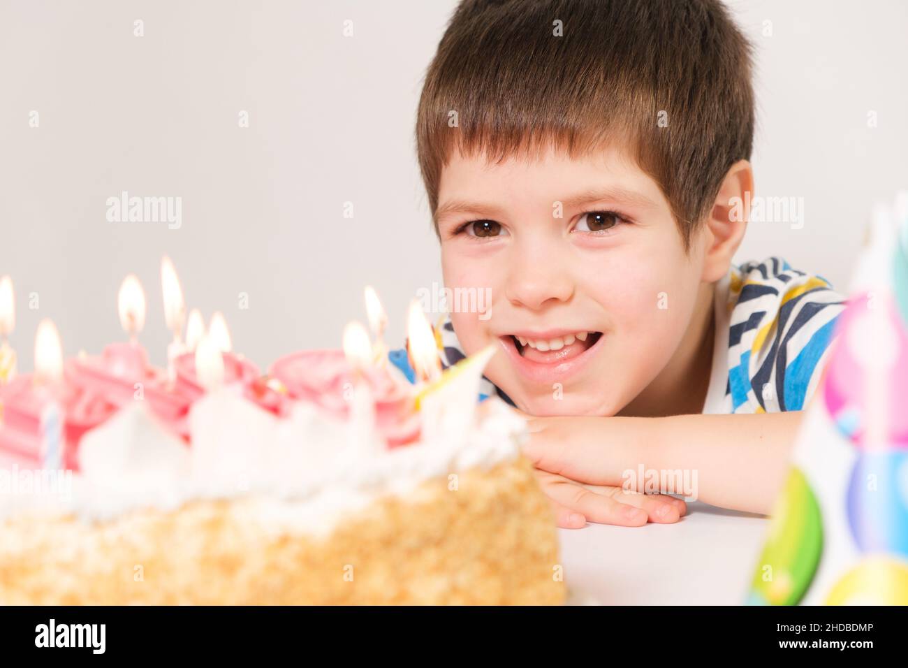 Ein kleiner Junge lacht, feiert seinen Geburtstag, sitzt mit Kerzen vor einem weißen Kuchen. Stockfoto