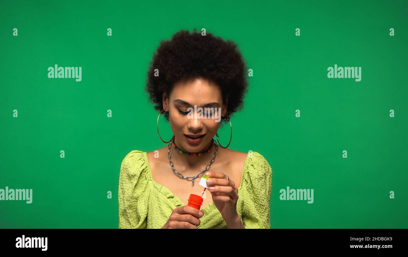 Lockige afroamerikanische Frau hält Flasche mit Seifenblasen isoliert auf grün Stockfoto
