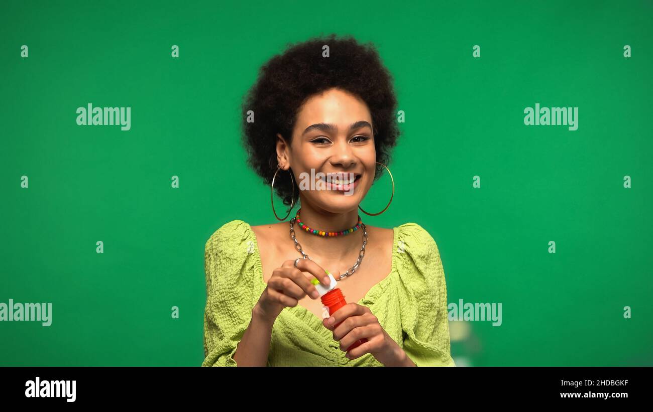 Fröhliche afroamerikanische Frau mit Flasche und Seifenstab isoliert auf grün Stockfoto