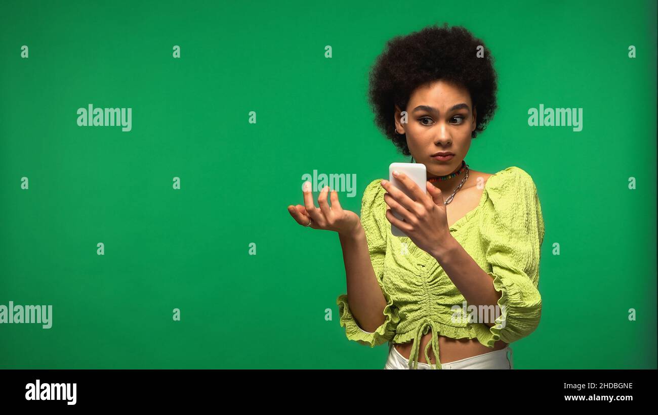 Unzufriedene afroamerikanische Frau mit Smartphone isoliert auf grün Stockfoto