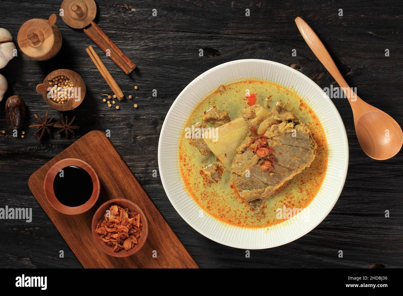 Blick von oben auf Gulai Kambing ist die traditionelle indonesische Hammelcurry-Suppe. Auf Schwarzem Holztisch Stockfoto
