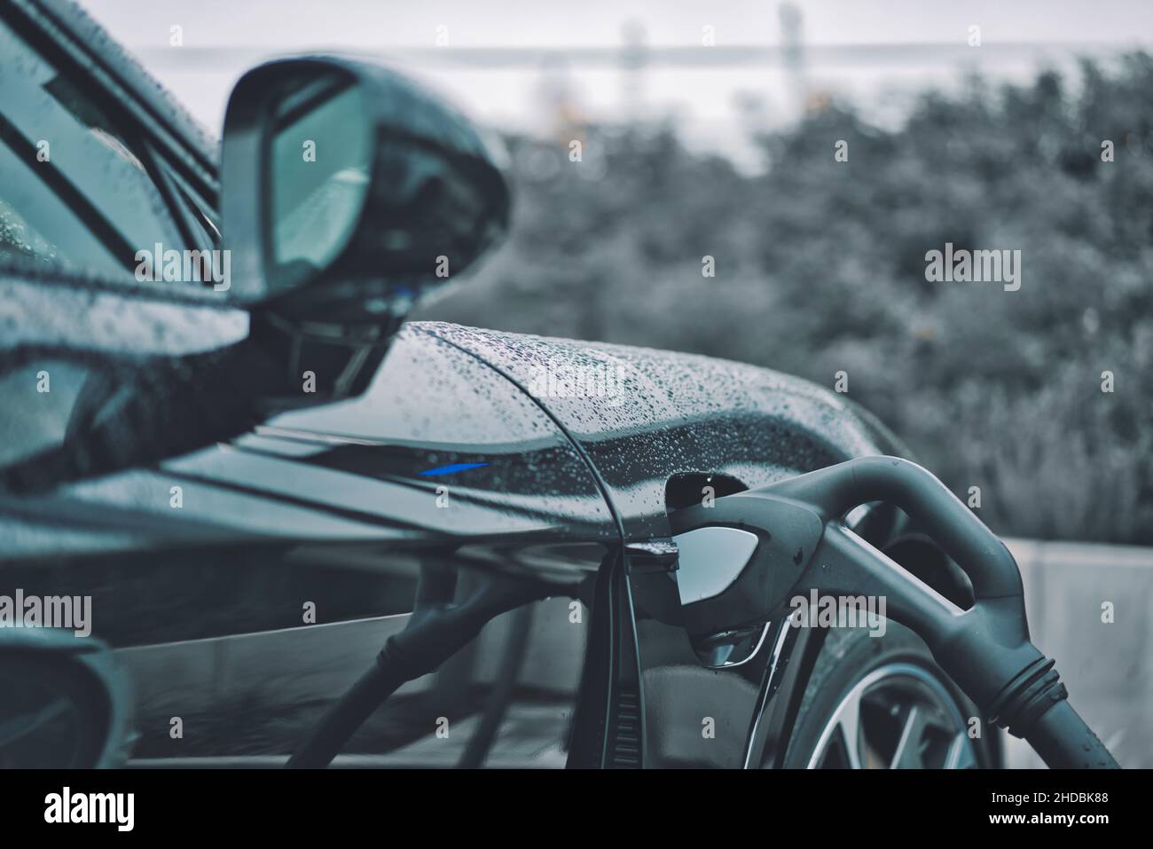 An einem regnerischen Tag füllt die Kraftstoffpumpe ein schwarzes Luxusauto mit Benzin in einer Tankstelle auf Stockfoto