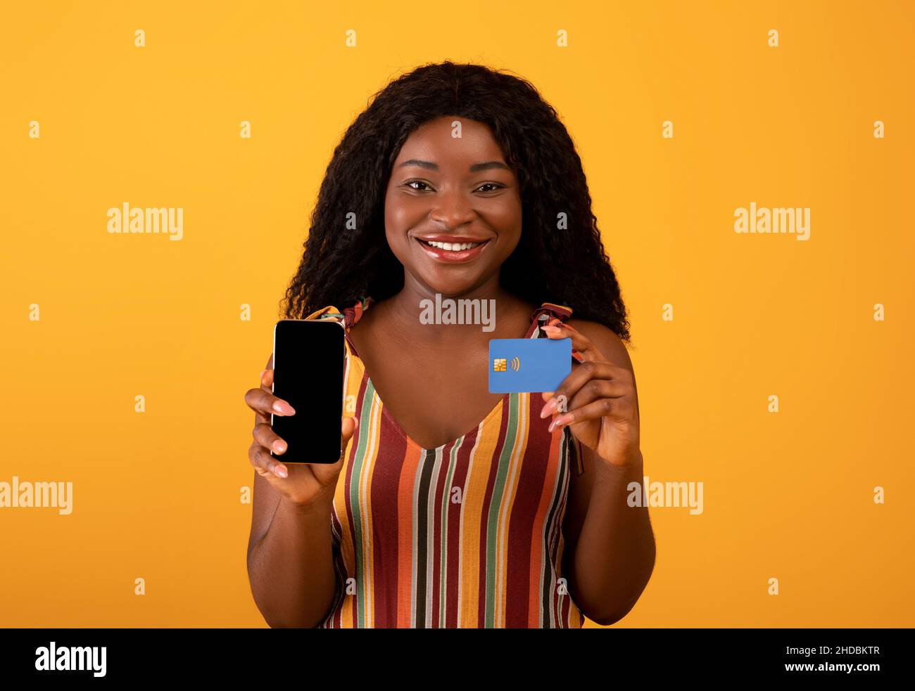 Neue tolle mobile Shopping-App. Fröhliche schwarze Frau zeigt Handy mit leerem Bildschirm und Kreditkarte Stockfoto