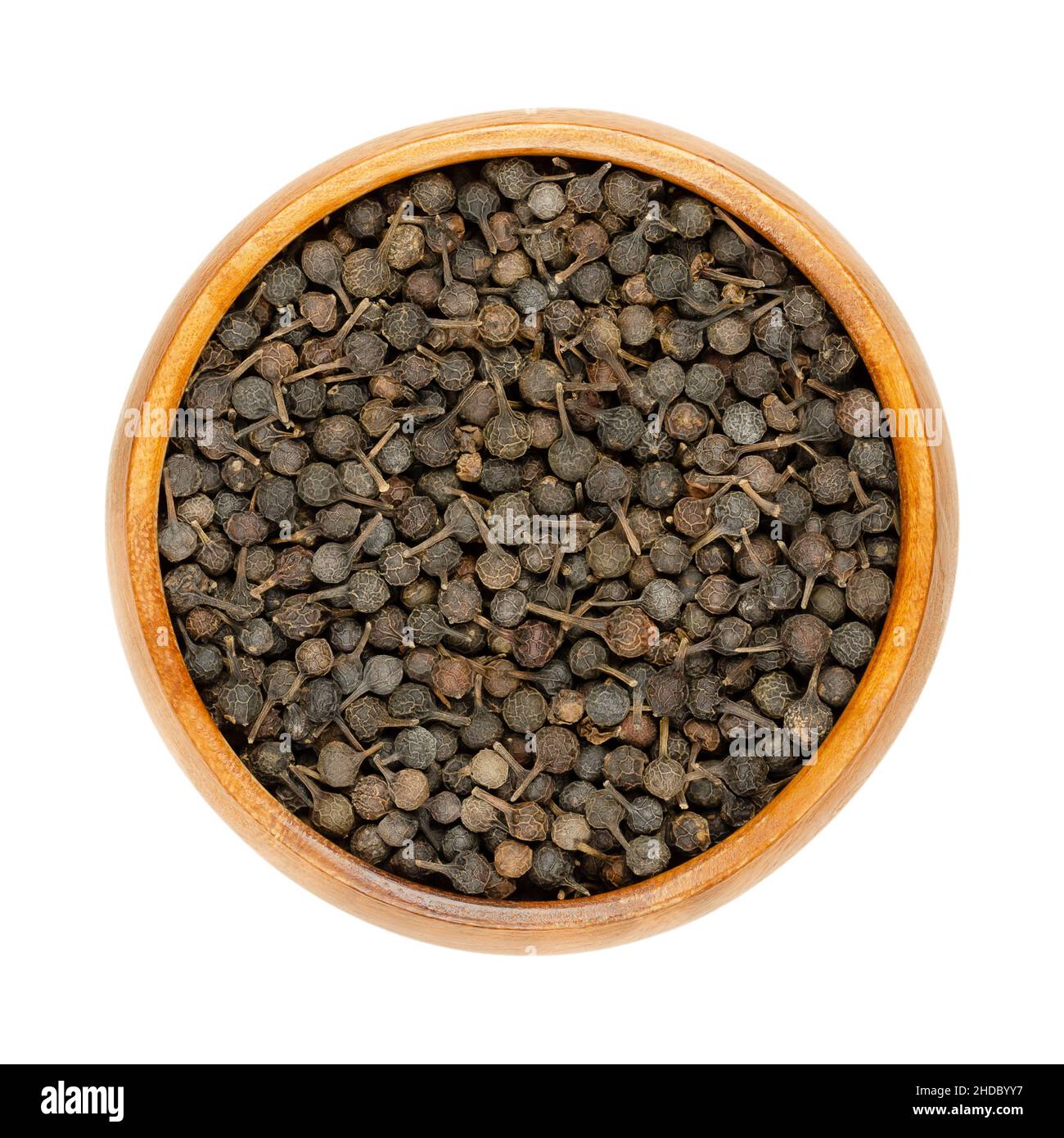 Cubeb Beeren bekannt als Schwanz Pfeffer oder Java-Pfeffer in Holzschüssel. Dunkelbraune Beeren mit ihren Stielen noch befestigt. Getrocknete Früchte von Piper cubeba. Stockfoto