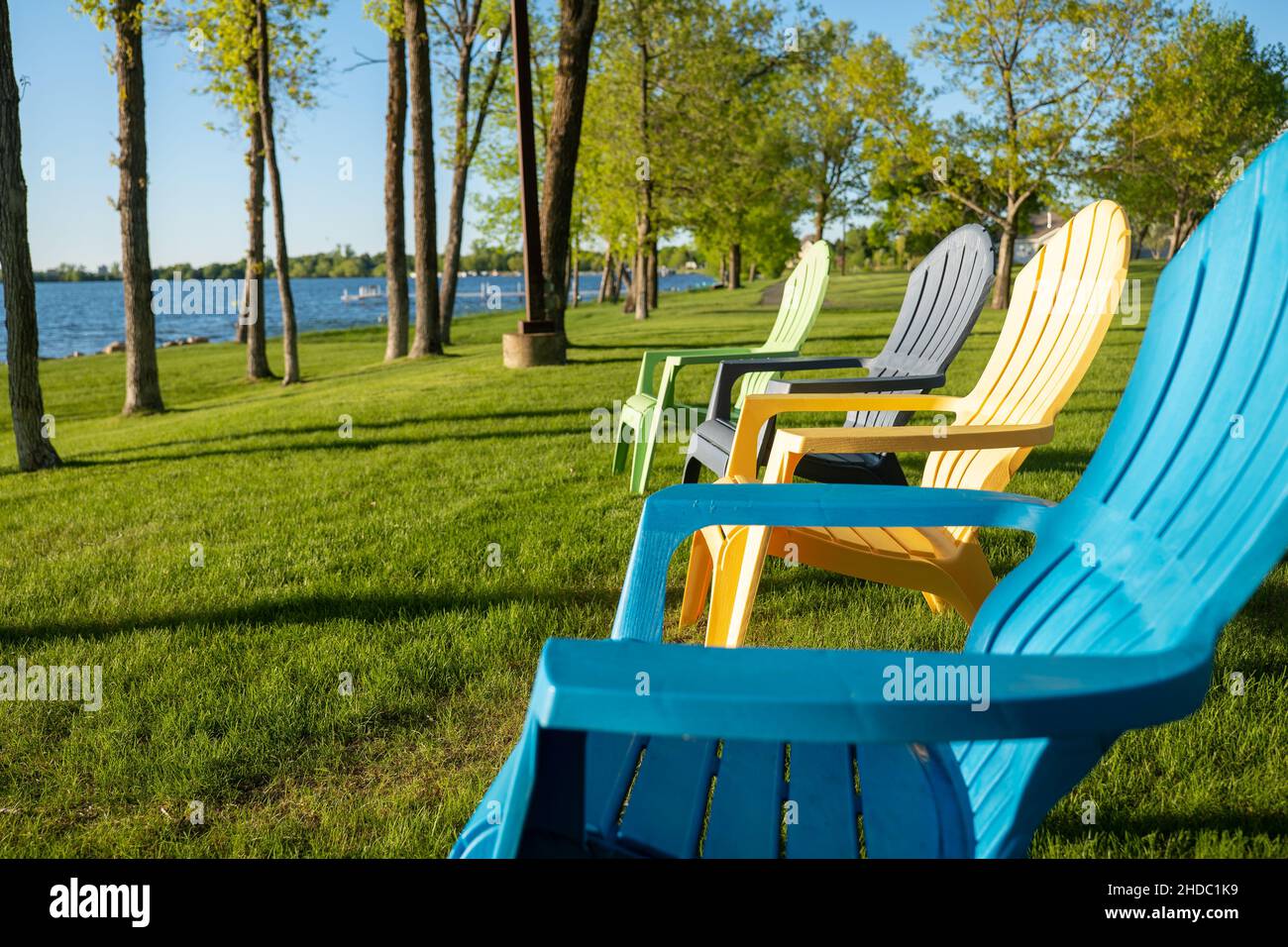 Farbenfrohe Adirondack-Stühle auf dem grünen Gras in der Nähe der Küste eines wunderschönen Minnesota-Sees an einem sonnigen Abend. Stockfoto