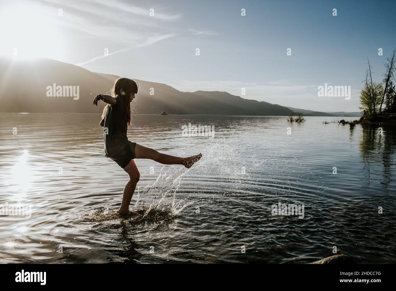 Junges Mädchen, das an einem See ins Wasser tritt und spritzt Stockfoto