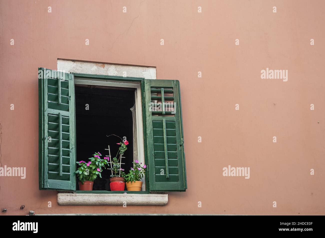 Ein Fenster mit geöffneten Fensterläden und Innenpflanzen auf der Fensterbank. Stockfoto