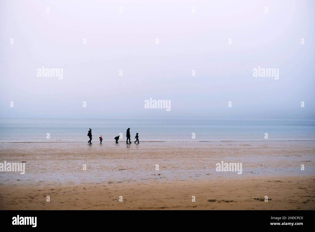 Eine Gruppe von zwei Erwachsenen und drei kleinen Kindern, die im Winter am Ufer von Scarborough spazieren gehen Stockfoto