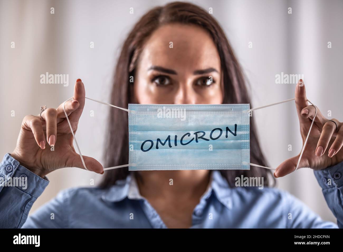 Eine junge Frau zieht eine Schutzmaske mit der Aufschrift Omicron an. Stockfoto