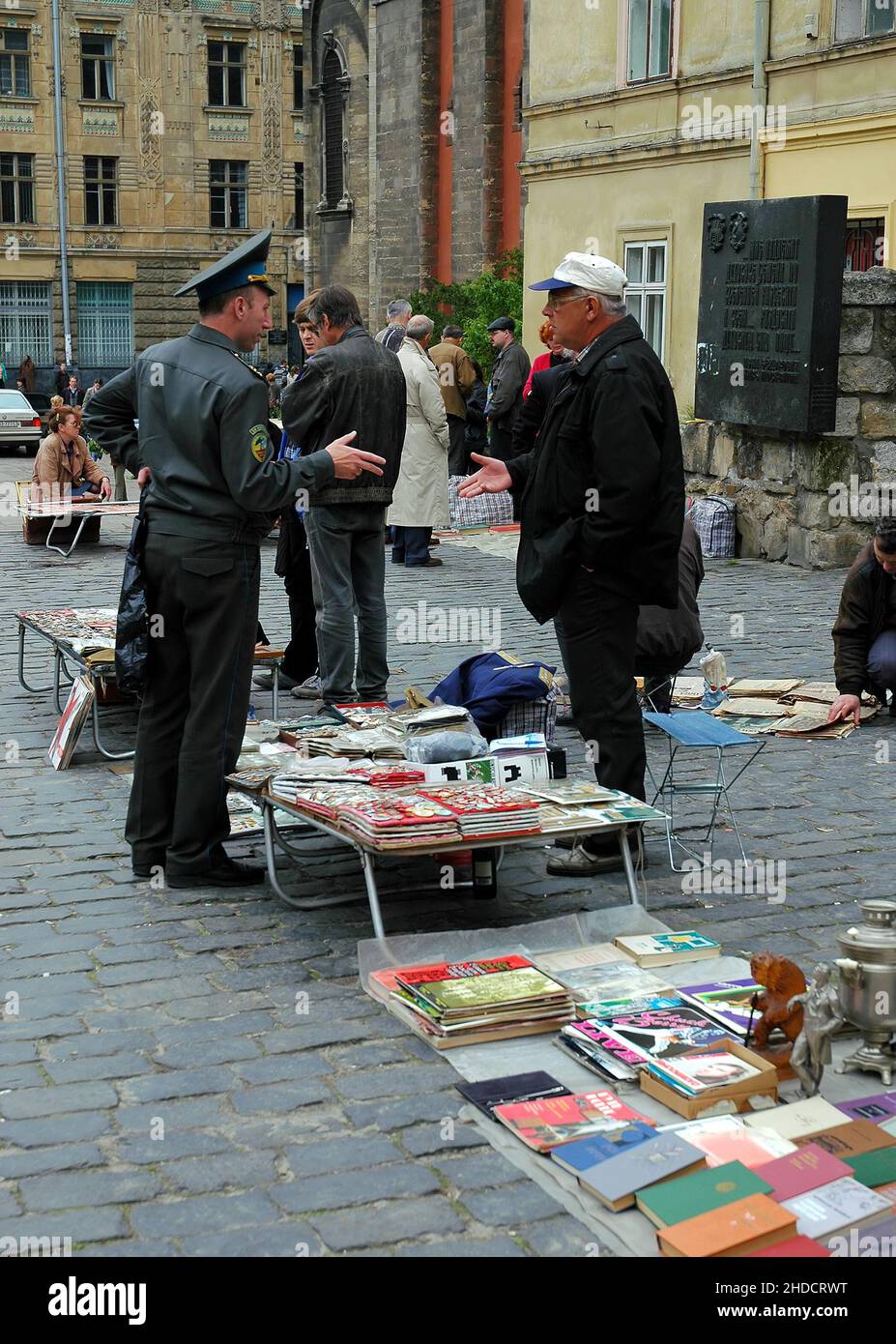 Lviv, Ukraine: Buchmarkt und Flohmarkt auf dem Muzeina-Platz hinter der Kirche der Heiligen Eucharistie. Ein Mann in Uniform spricht mit einem Stallhalter. Stockfoto