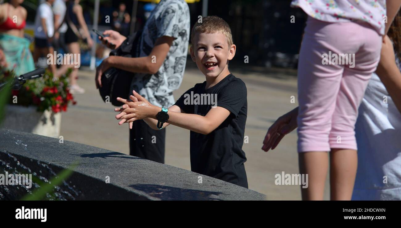 Kinder am Brunnen. Ein achtjähriger Junge macht sich zwischen den Wasserbächen im Springbrunnen lustig. Sommer in der Stadt an einem heißen Tag. Stockfoto