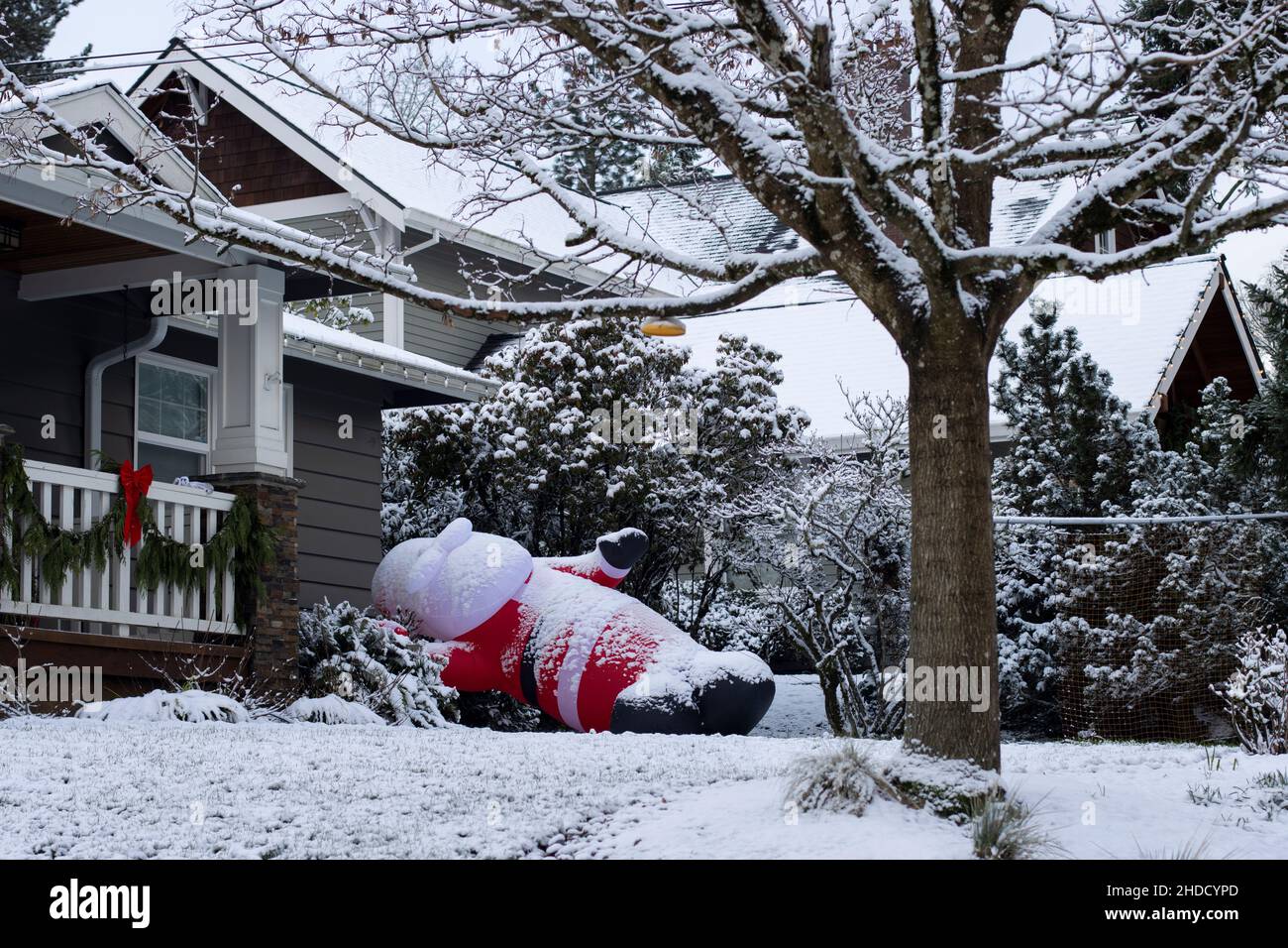 Aufblasbarer Weihnachtsmann fällt im Vorgarten nach über Nacht starken Winden und Schnee während der Winterferiensaison. Stockfoto