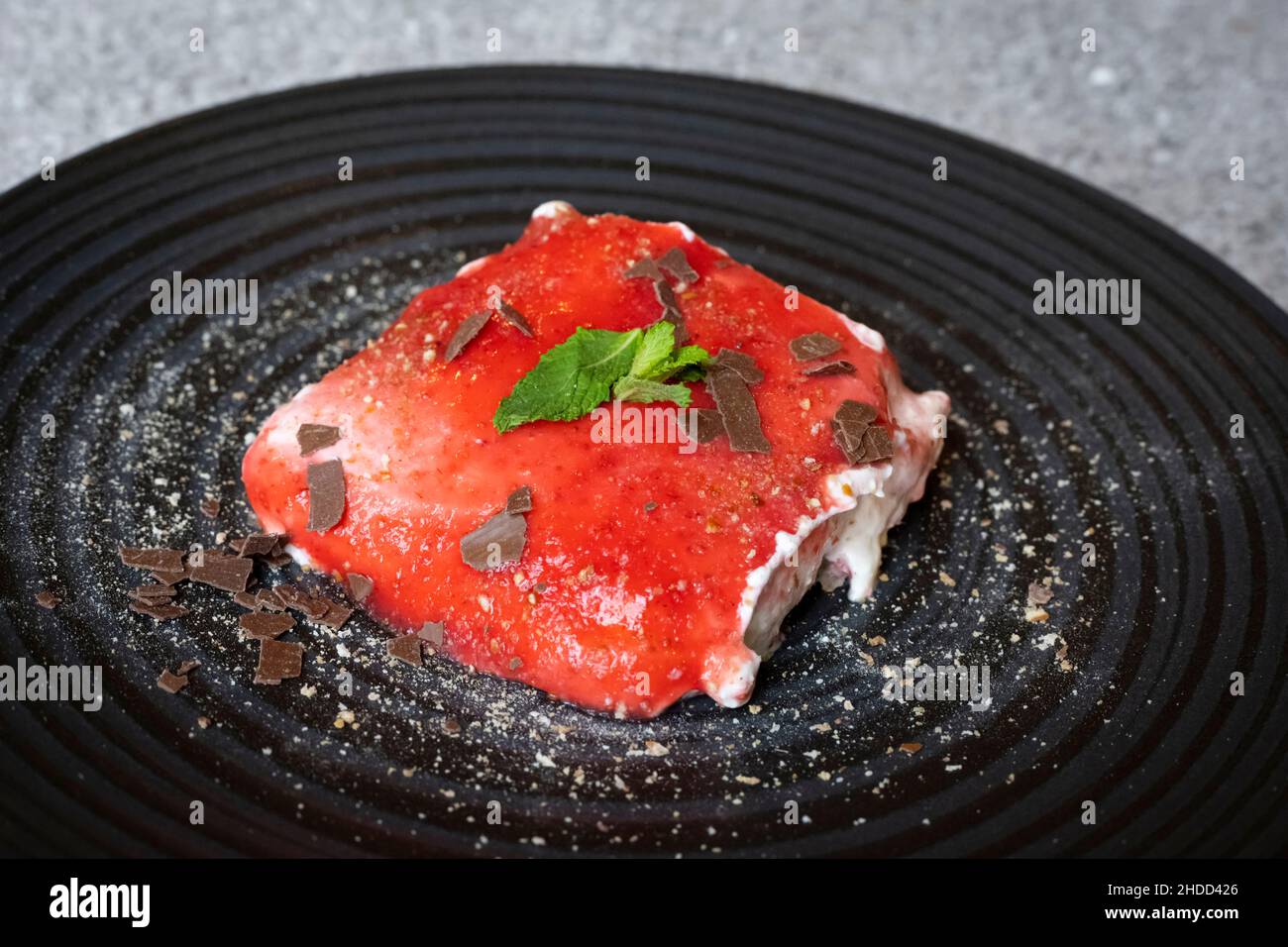 Herzhafte Erdbeer-Tiramisu auf einem schwarzen Teller mit Pfefferminze, Puderzucker und Schokoladenstreuseln Stockfoto