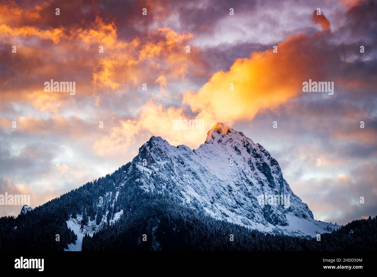 Extrem brennende Wolken am Abendhimmel über der gehrenspitze mit frisch verschneiten Felsen im Herbst Stockfoto