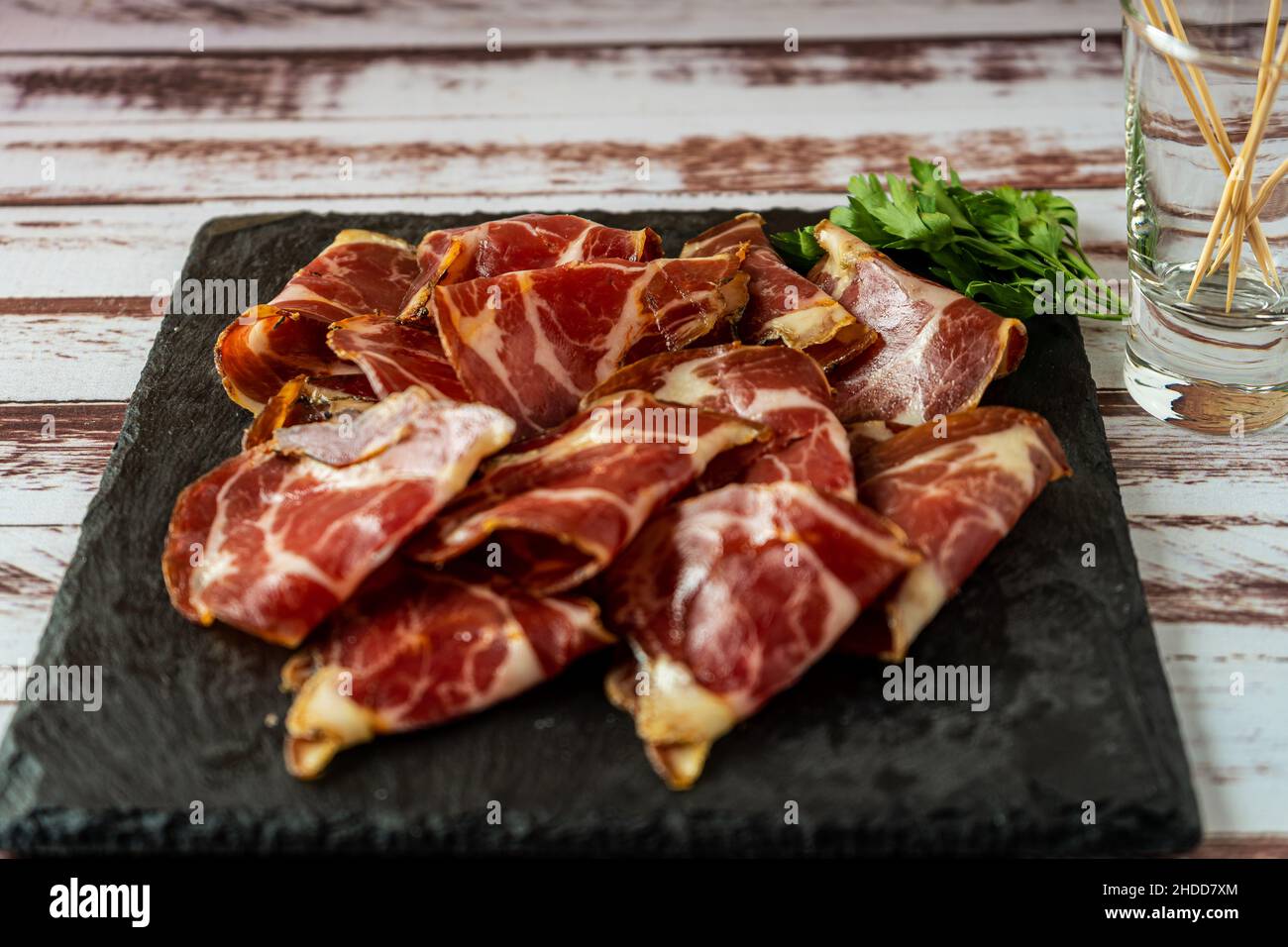 Zerkleinerte Ansicht eines exquisiten Fetas de Bondiola oder rohes eingelegtes Schweinefleisch auf einer schwarzen Platte. Stockfoto