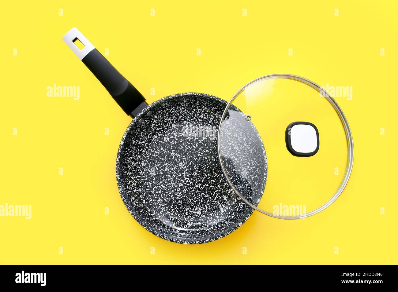 Schwarze Bratpfanne mit Glasdeckel auf gelbem Hintergrund, Draufsicht Stockfoto