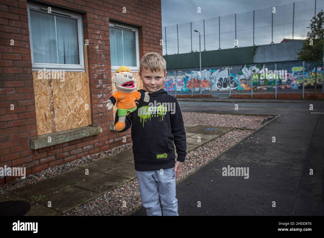 Kleiner Junge mit Spielzeug und Friedensmauer, die in Belfast entlang läuft und überwiegend republikanische und nationalistische katholische Viertel trennt. Stockfoto