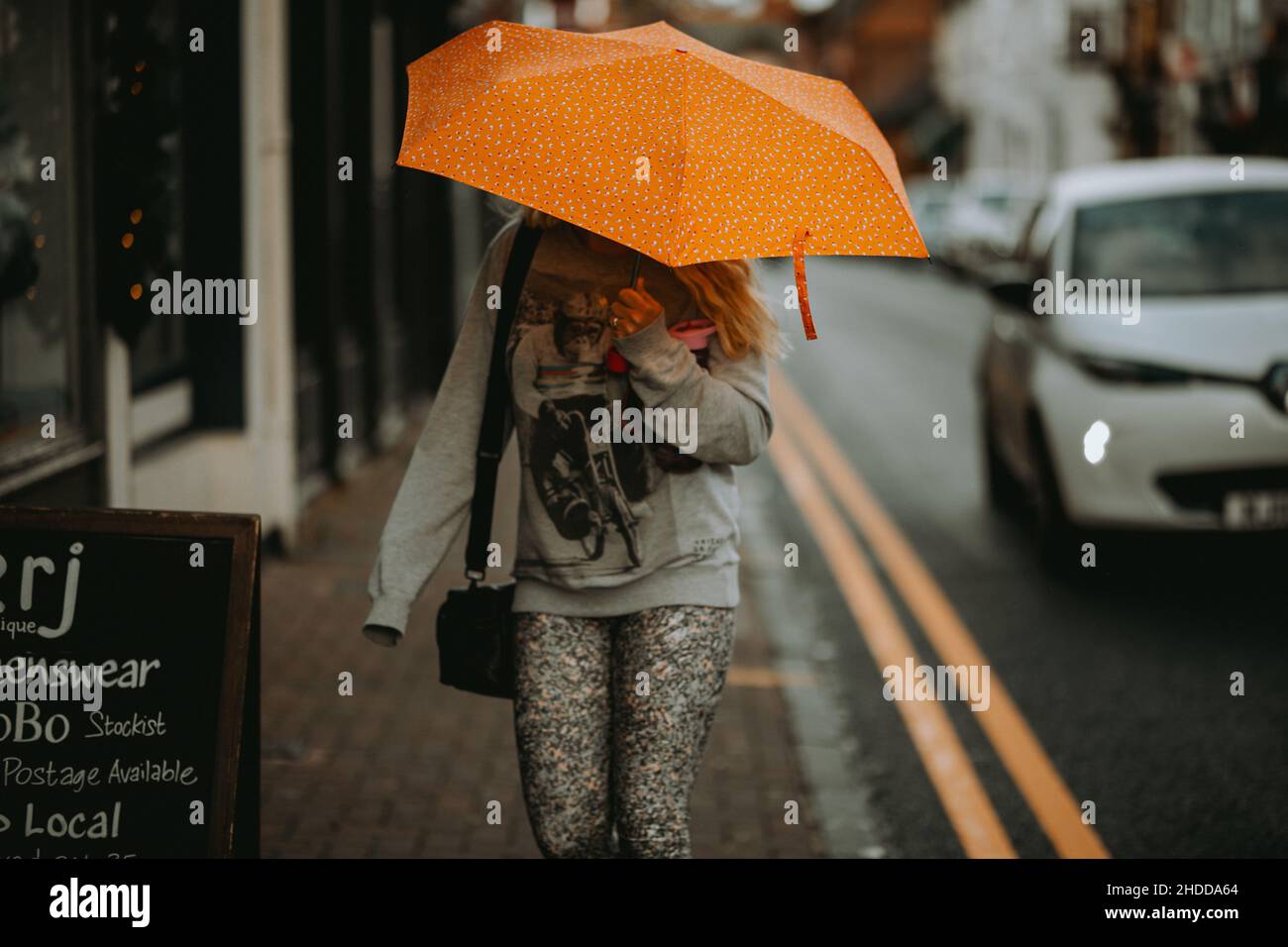 Weibchen mit einem orangenen Regenschirm, der in einer Stadt spazierengeht Stockfoto
