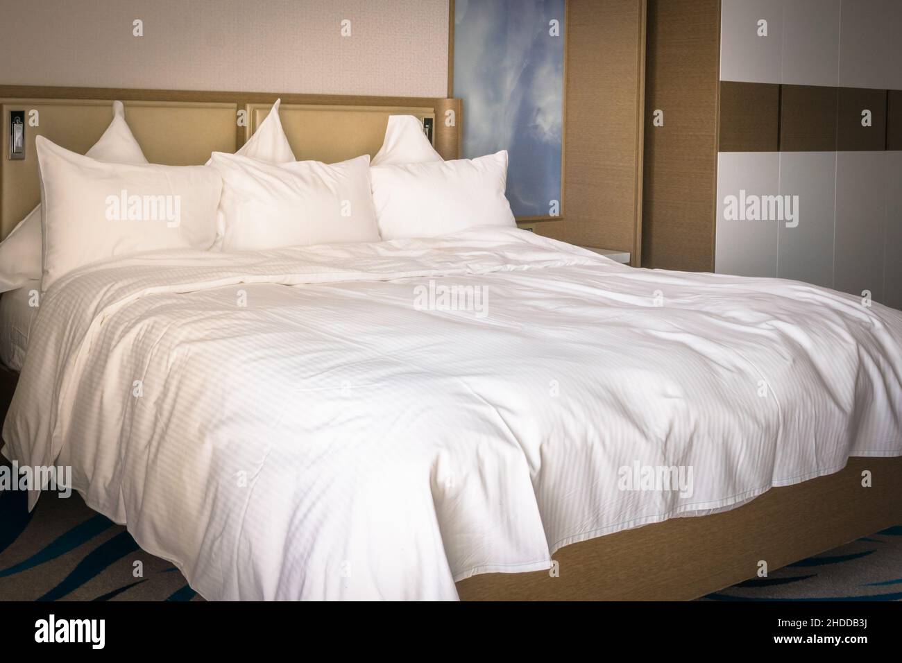 Kingsize-Bett mit brauner Innenausstattung und weißen, hellen, sauberen Laken und sechs Kissen. Luxuriöse Aufenthalte und Komfortkonzept. Stockfoto