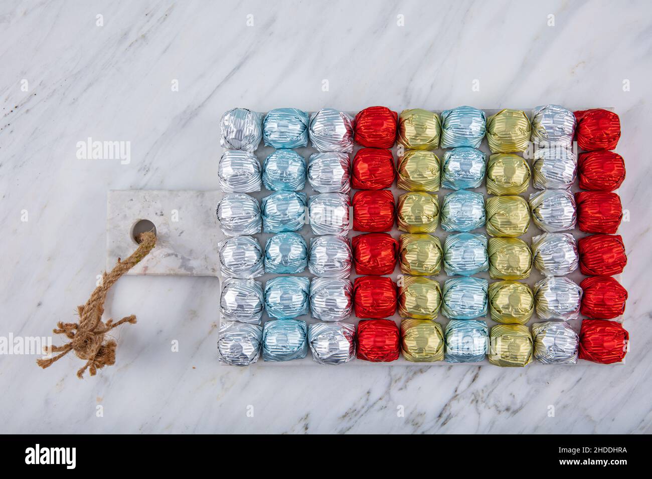 Runde Schokoladenkugeln mit Aluminiumfolie in Box-Behälter auf Marmorboden. Minimalistische, festliche Frühlingskomposition. Weicher selektiver Fokus, Stockfoto