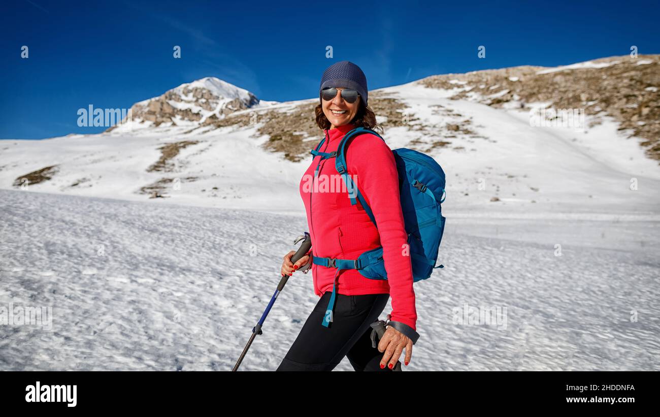 Halblanges Porträt einer lächelnden Frau, die an einem sonnigen Wintertag allein auf dem Schnee in den Bergen unterwegs ist. Sportperson im Schnee. Horizontal Stockfoto