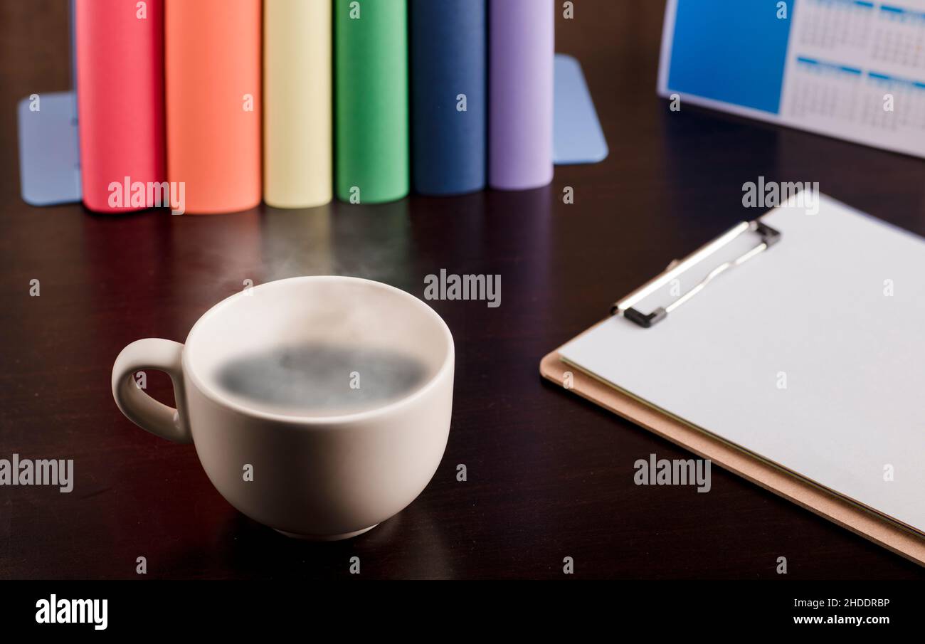 tasse Kaffee oder Tee mit heißem Dampf, Bücher mit lgtbi-Flaggen auf dem Schreibtisch. Stockfoto