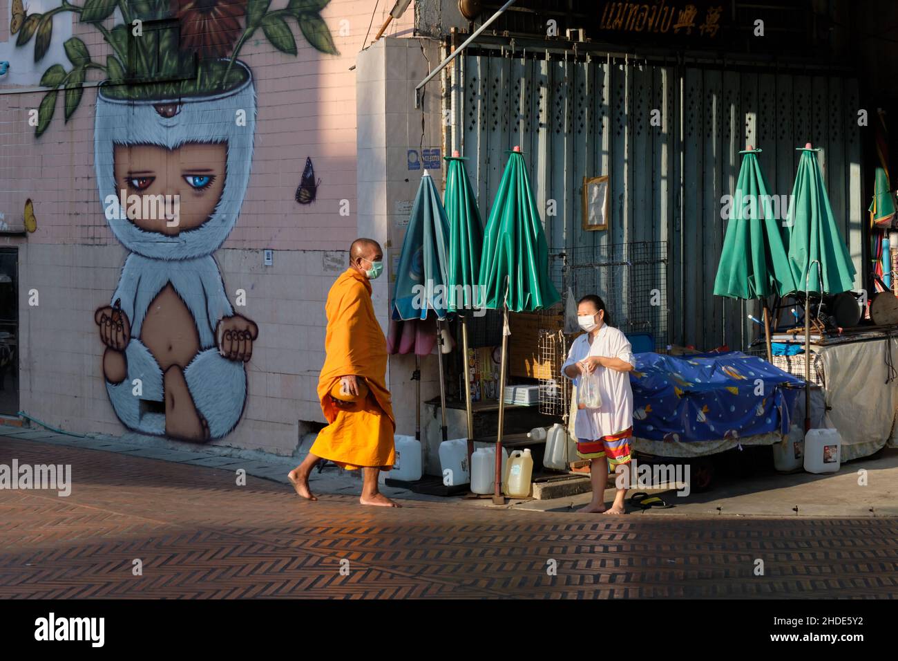 Eine Frau geht zu einem großen buddhistischen Mönch über, auf dem ein meditierender Charakter dargestellt ist; Klong Ong Ang Walking St., Pahurat/Chinatown, Bangkok, Thailand Stockfoto