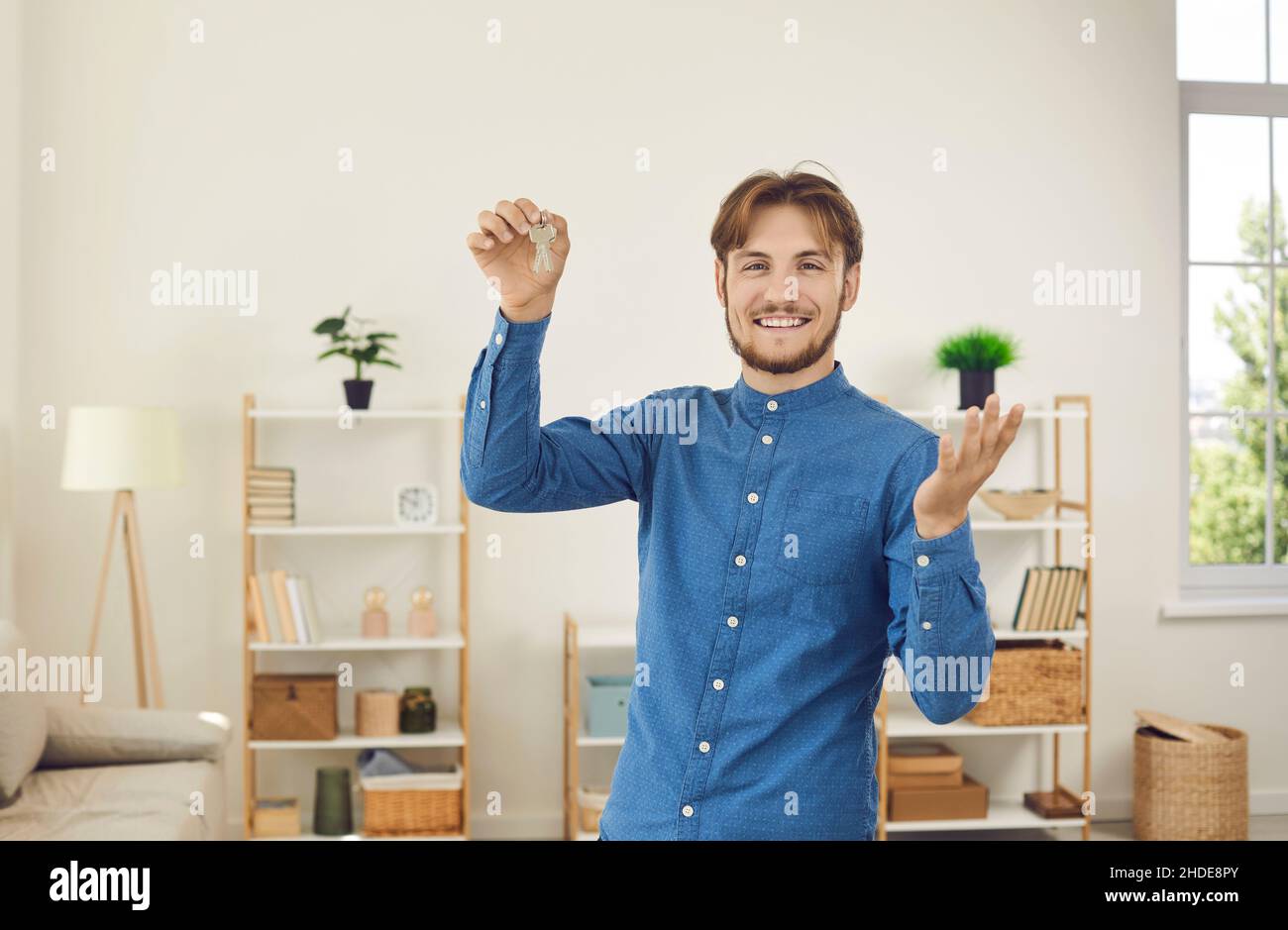 Glücklicher männlicher Hausbesitzer, der sich mit dem erfolgreichen Immobilienkauf rühmt und Schlüssel zu seinem neuen Zuhause zeigt. Stockfoto