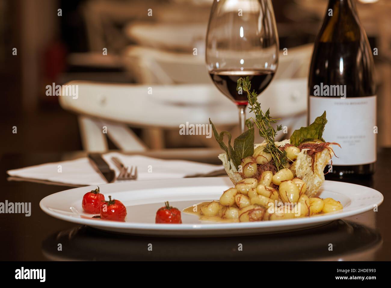 Ein appetitliches Teller mit hausgemachten Gnocchi und einem Glas Rotwein sowie ein paar Tische aus einem guten italienischen Restaurant. Stockfoto