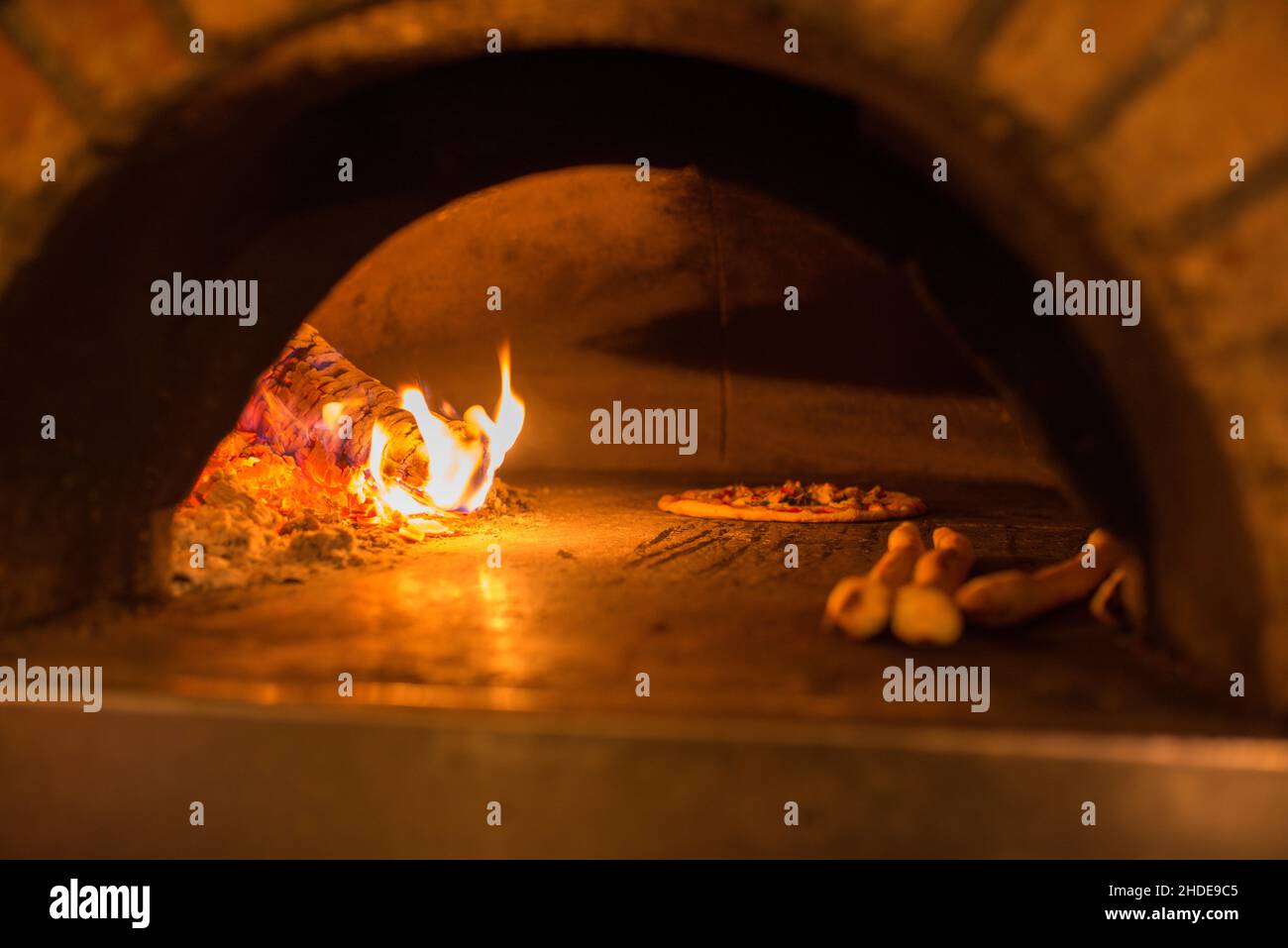Eine Pizza und ein Pizzabrot werden in einem Pizzaofen gebacken, der mit glühendem und brennendem Holz befeuert wird. Stockfoto