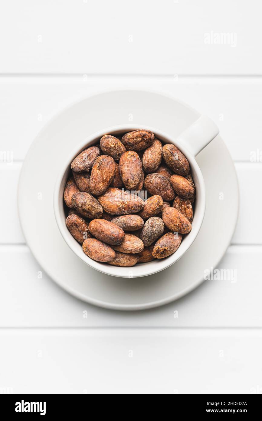 Getrocknete Kakaobohnen. Kakaobohnen in Tasse auf weißem Tisch. Stockfoto