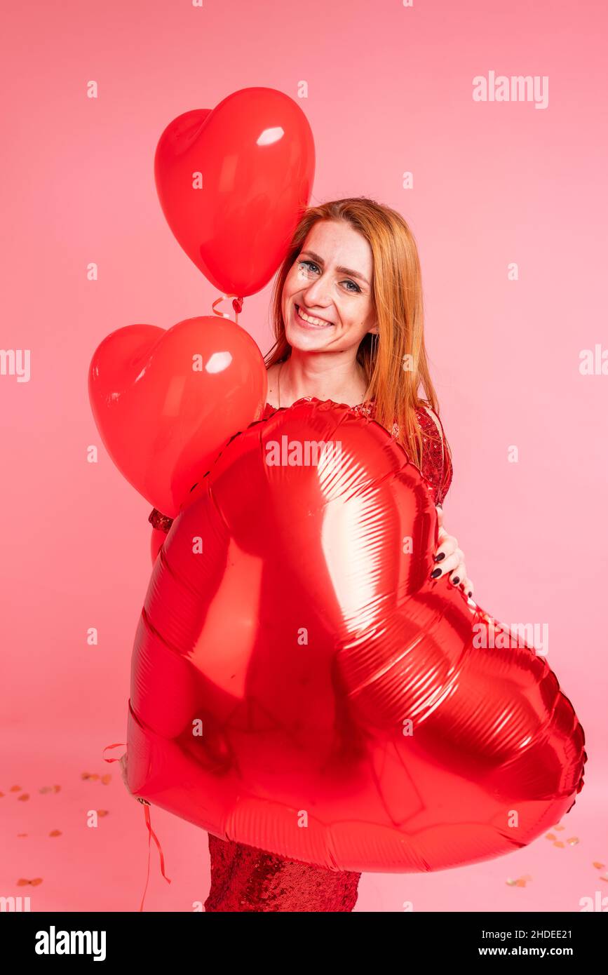 Schöne rothaarige Mädchen mit rotem Herz Ballon posiert. Alles Liebe zum Valentinstag Konzept. Studio Foto von schönen Ingwer Mädchen tanzen auf rosa Hintergrund. Stockfoto