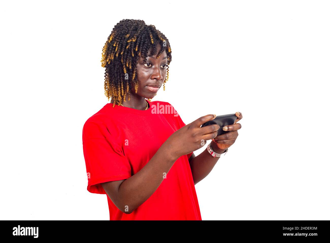 Eine schöne junge Frau in einem roten T-Shirt, die auf einem weißen Hintergrund mit dem Handy steht und wegschaut. Stockfoto