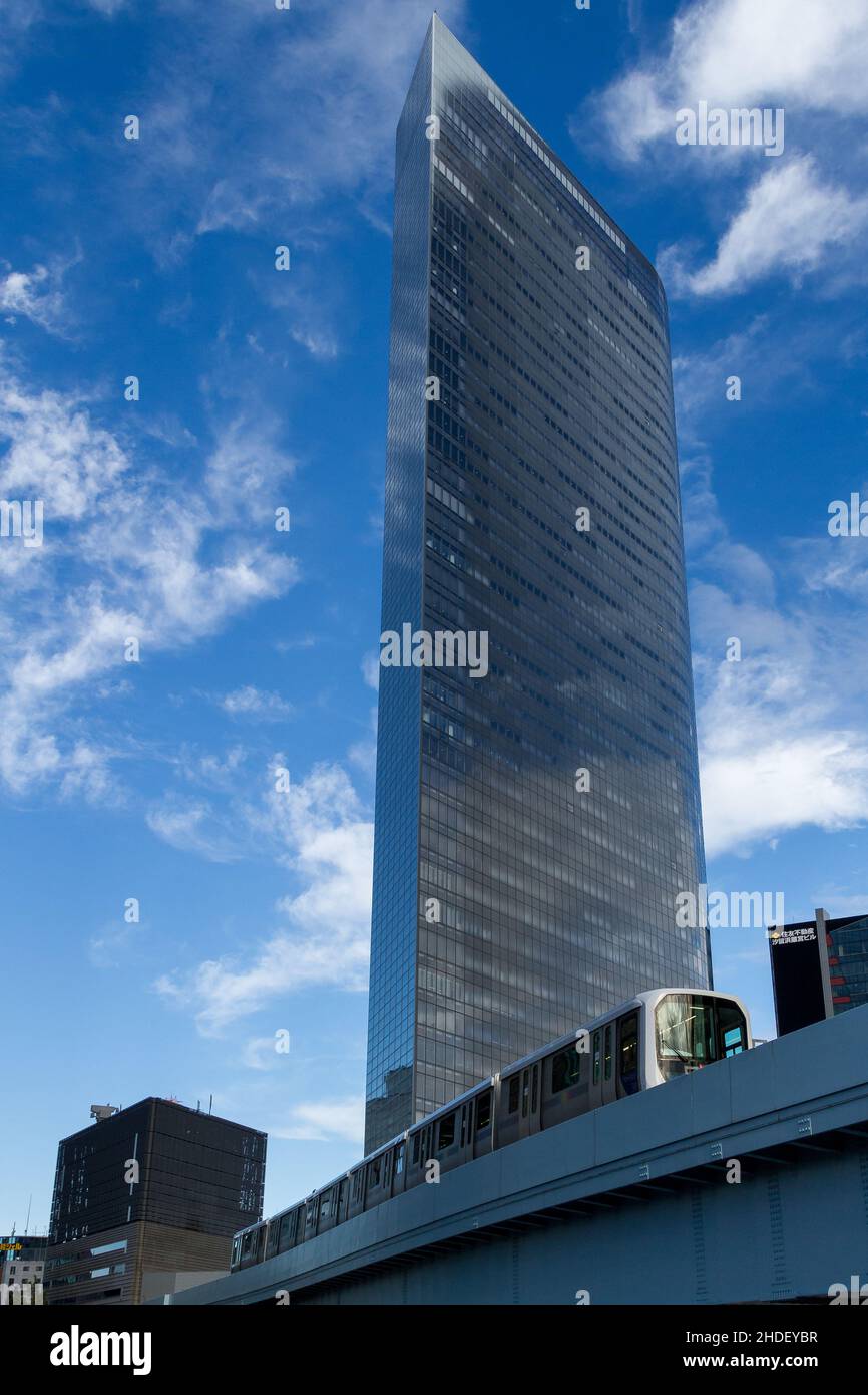 Das Dentsu-Gebäude in Shiodome mit einem Yurikamome Line-Zug, der darunter vorbeifährt. Shimbashi, Tokio, Japan. Stockfoto