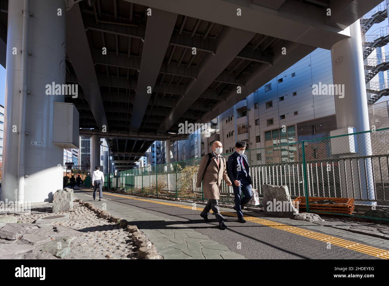 Salarymen, die chirurgische Masken gegen COVID-19 tragen, gehen unter einer Schnellstraße in Iidabashi, Tokio, Japan. Stockfoto