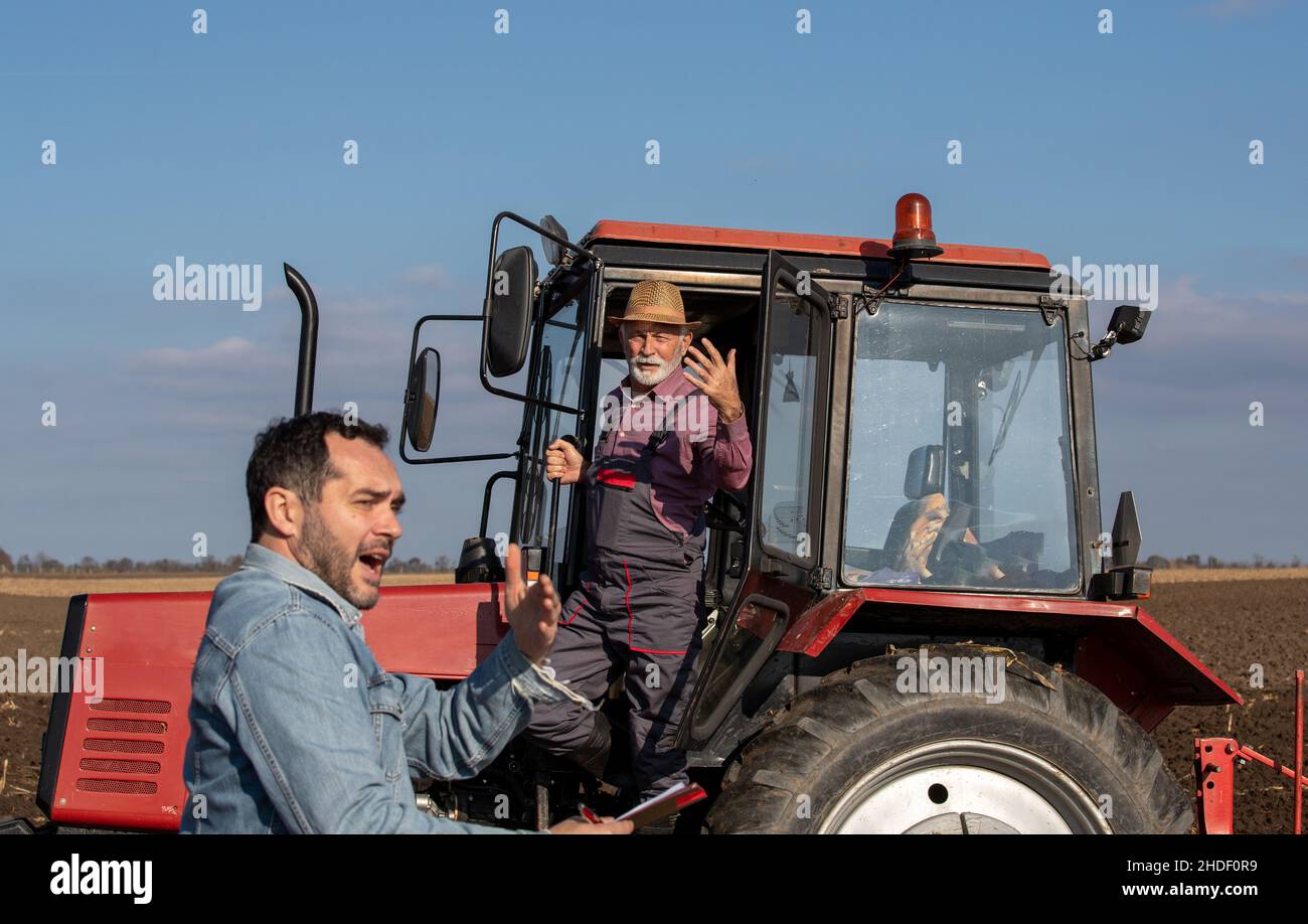 Älterer Mann, der einen Traktor fährt und mit einem Landarbeiter auf einem Bio-Bauernhof streitet. Stockfoto