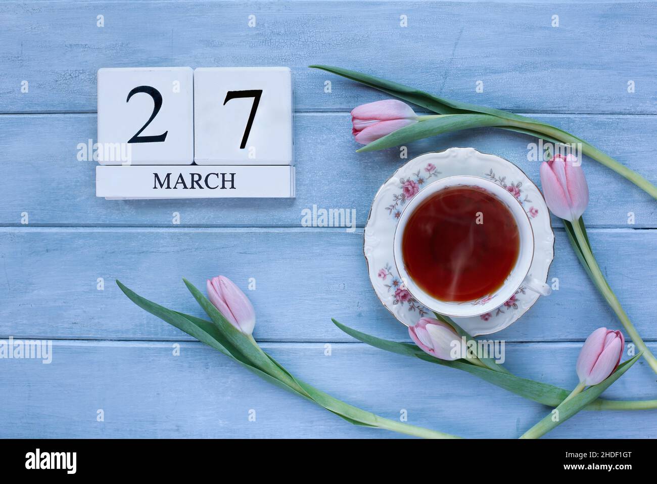Weiße Holz-Kalenderblöcke mit dem Datum März 27 und rosa Tulpenblumen mit Tee auf blauem Holzhintergrund für den Muttertag in Großbritannien. Stockfoto
