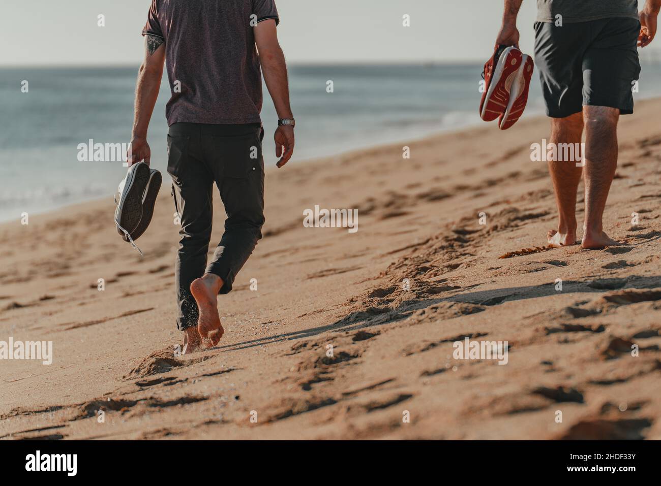 Zwei Leute, die mit ihren Schuhen in der Hand am Orange County Newport Beach spazieren Stockfoto