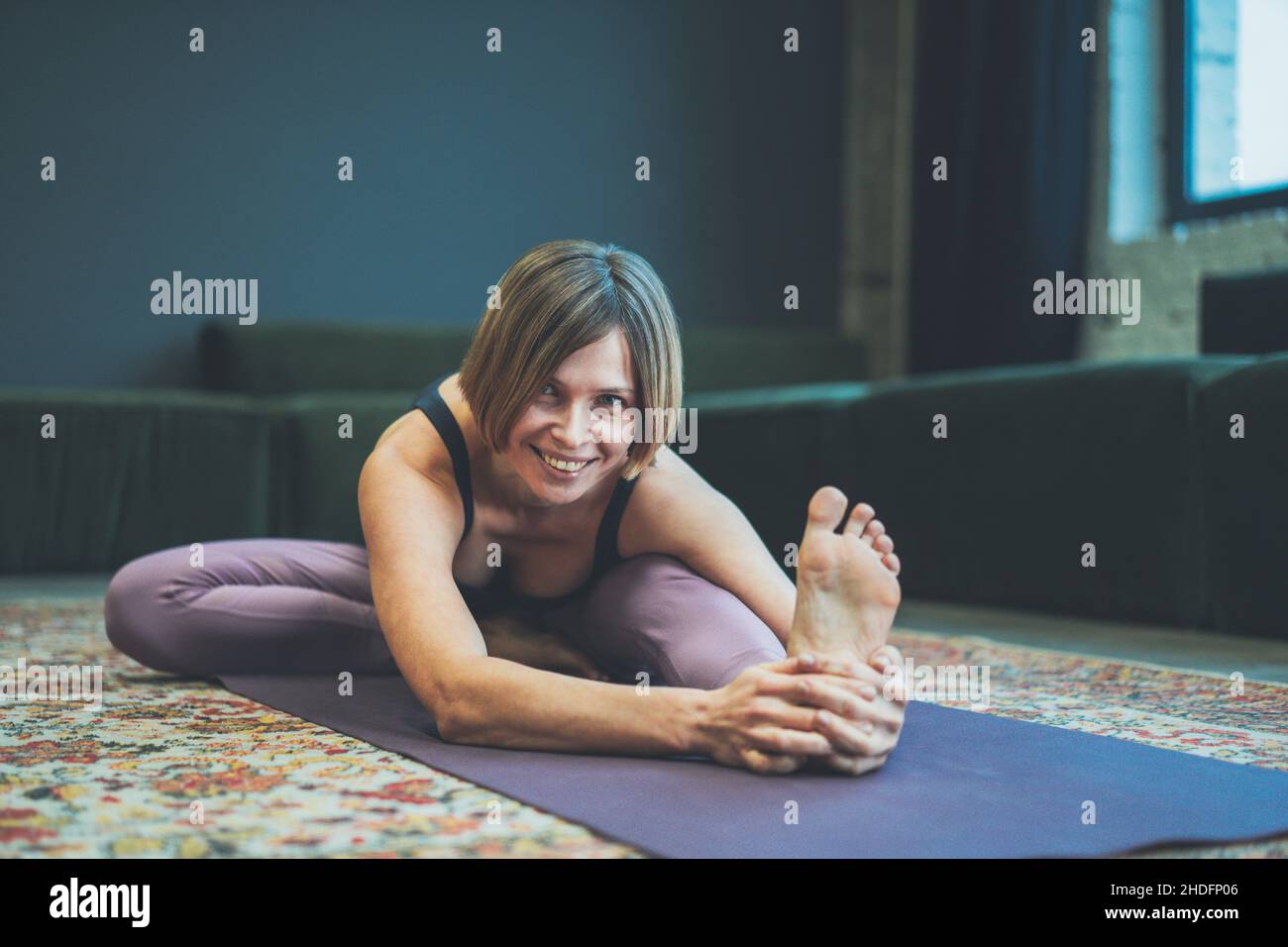 Lächelnde junge Frau auf einer Matte tut ein Asana. Konzept des Yoga in der Stadt. Gesundheit, Langlebigkeit, schlanke Figur. Hochwertige Fotos Stockfoto