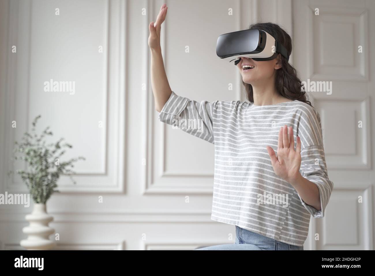 Junge glückliche Frau im Virtual-Reality-Headset, die Spaß beim Einkaufen in der erweiterten Welt hat Stockfoto