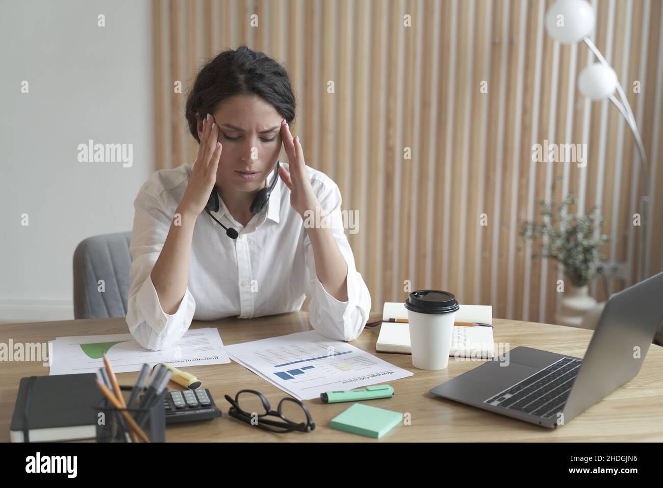 Frustriert verärgert italienerin, die den Kopf in den Händen hält und nach einem harten Arbeitstag Kopfschmerzen hat Stockfoto