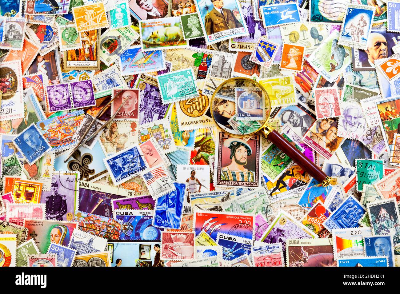 Stempelzange und Lupe auf einem Stapel von Briefmarken aus der ganzen Welt. Stockfoto