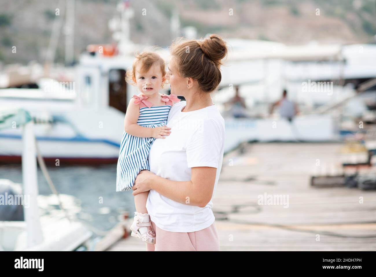 Mutter mit Baby Mädchen 1-2 Jahre alt mit Strohhut über Meer und Boote im Hintergrund aus nächster Nähe. Familienleben. Sommersaison. Kindheit. Stockfoto