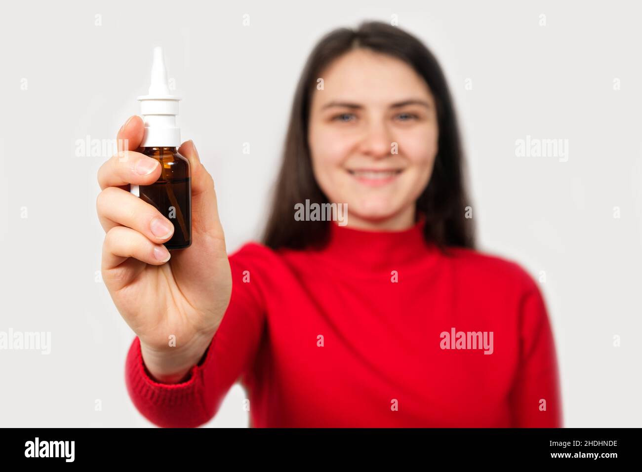 Eine brünette Frau in rot zeigt eine Flasche Nasenspray zur Behandlung von Rhinitis und Allergien Stockfoto